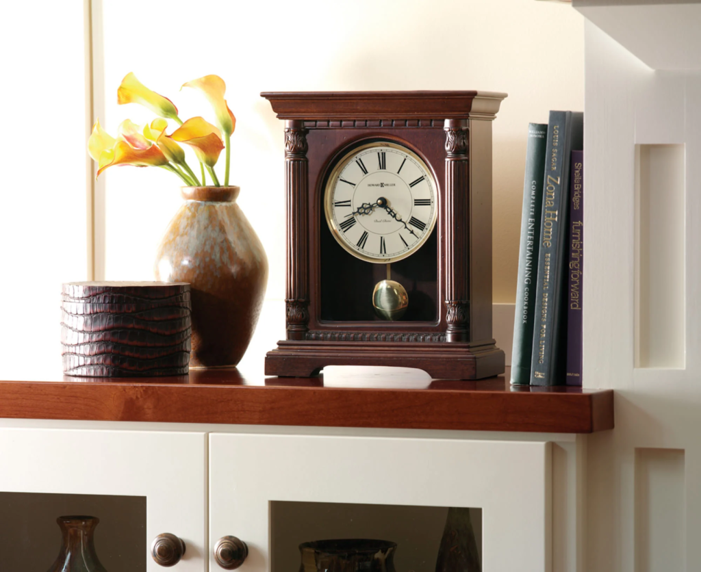 Clock chimes on a shelf next to books and a vase