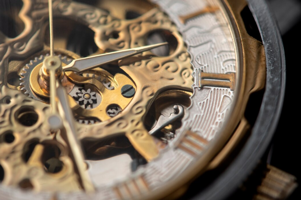 A close-up view of intricate golden clockwork components, with detailed carvings and gears, highlighted by the sheen of polished metal